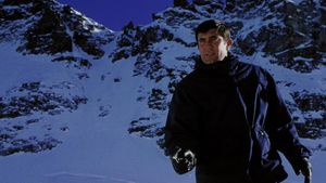 James Bond, warmly dressed, is standing against a backdrop of snowy mountains. He is pointing a gun at someone off screen.